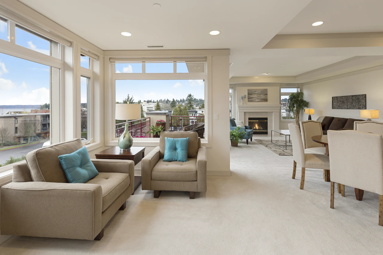 A furnished apartment living room with large windows and teal cushions